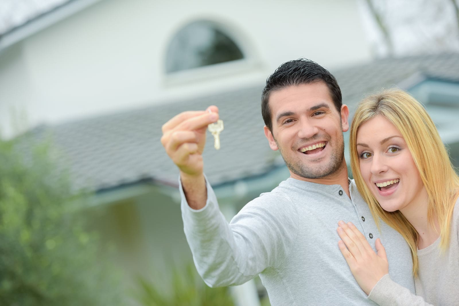Smiling couple holding house keys outside their new home, celebrating a property purchase with no transfer tax.