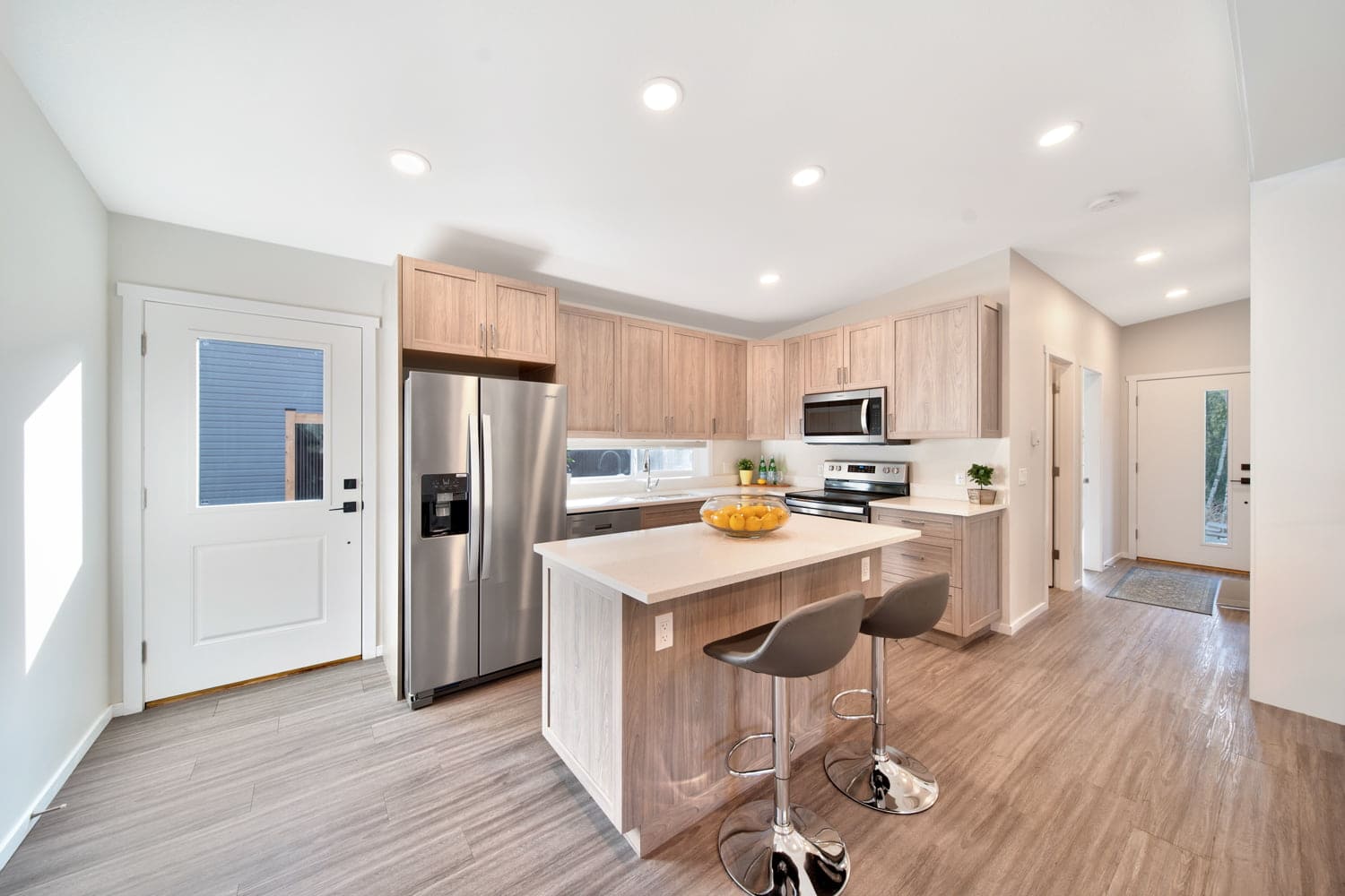 Modern kitchen with wood cabinetry, stainless steel appliances, and two bar stools at a central island, showcasing a fully move-in-ready layout.